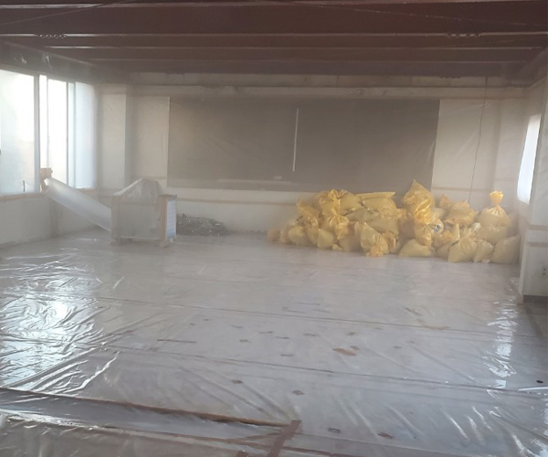 室内には負圧除じん装置とアスベストが入った専用の廃棄袋が積みあがっており、鉄骨の天井から吹き付けアスベストが除去されている