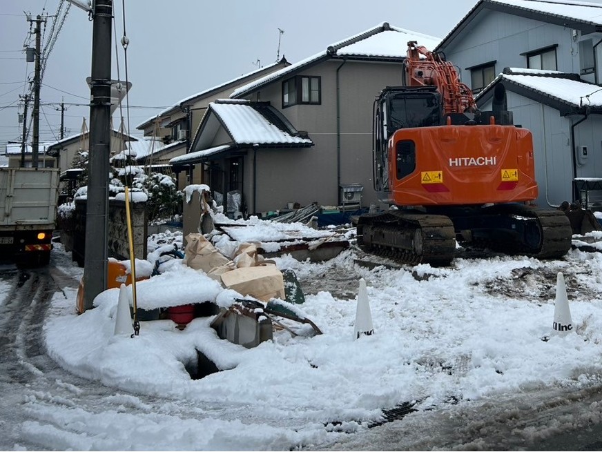 雪の中で重機を用いて解体工事を行っています。
