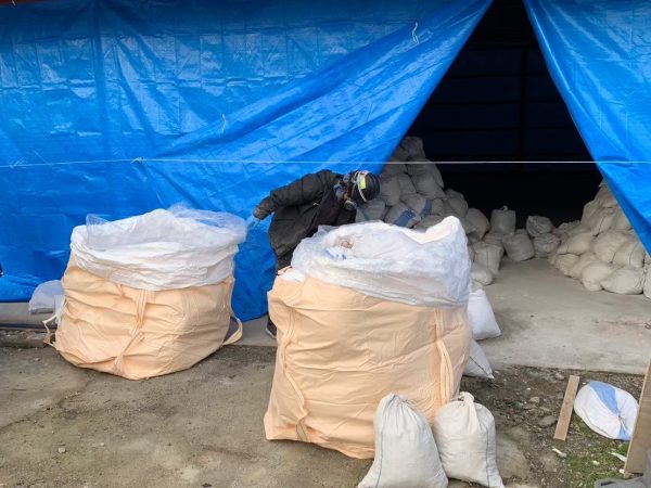 富山のアスベスト解体現場で、株式会社エイキの作業員が、廃材が詰められた小さな袋をフレコンバックに詰めている様子。